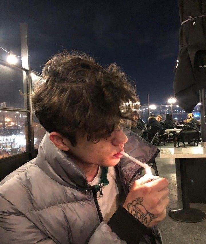 a young man is drinking from a cup outside at night with the city lights in the background