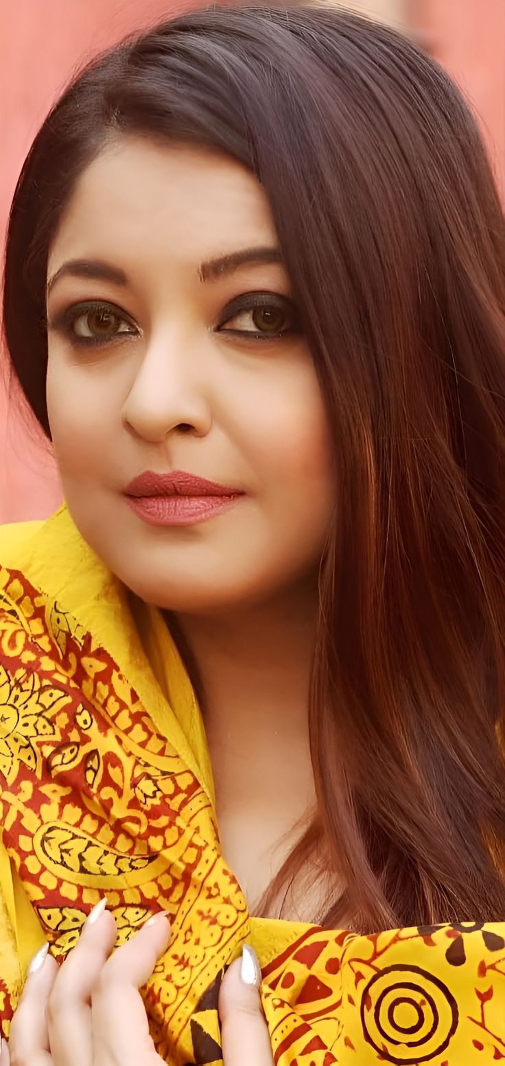 a woman with long brown hair wearing a yellow and red scarf over her shoulders, posing for the camera