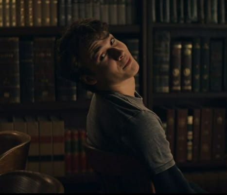 a young man sitting in front of a bookshelf with his head turned to the side