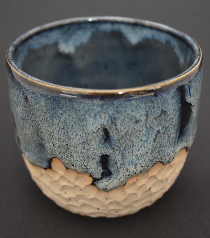 a close up of a cup on a black surface with blue and white glaze