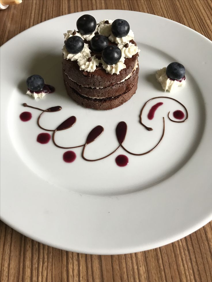 a white plate topped with a chocolate dessert covered in blueberries and whipped cream on top of a wooden table