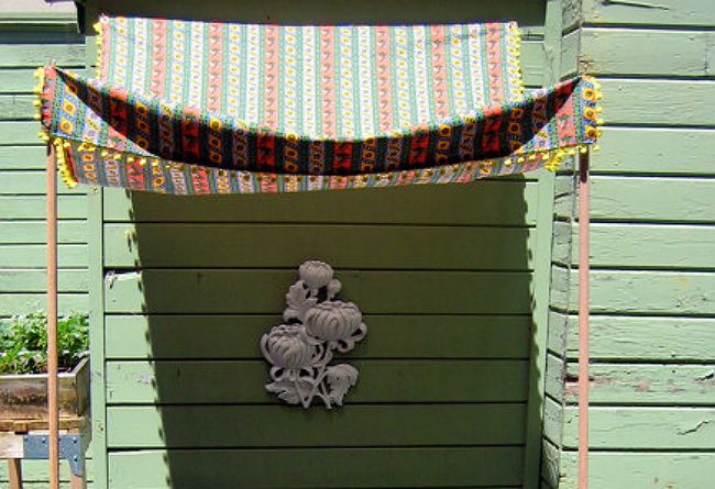 a green house with a decorative wall hanging on the front door and an awning over it