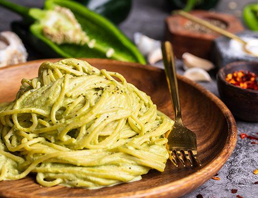 a wooden bowl filled with green pasta on top of a table