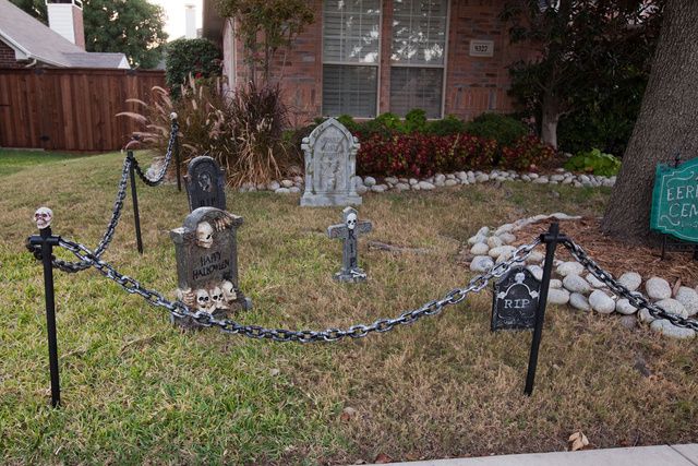 a cemetery with tombstones and chains in front of a house that has been decorated for halloween