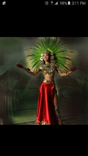 a woman in a red and gold costume with green feathers on her head, holding two hands out