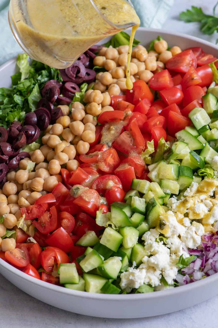 a bowl filled with salad and dressing being drizzled over the side dish