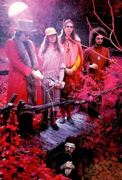 three people standing on a wooden bridge in the woods with trees and leaves around them