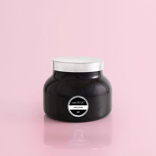 a black candle with a white lid on a pink background