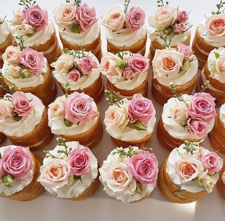 a table topped with lots of cupcakes covered in white frosting and pink flowers