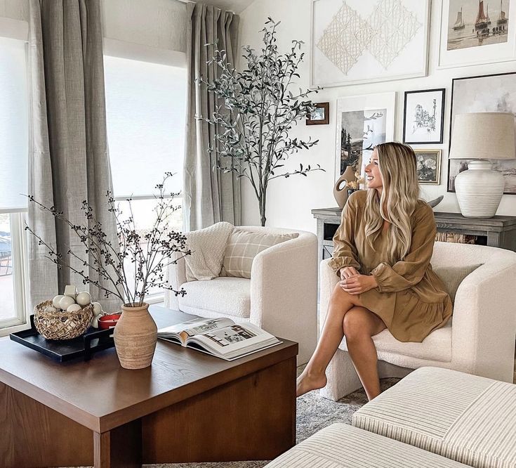 a woman sitting in a living room next to a couch and coffee table with pictures on the wall