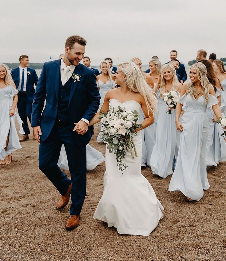 a bride and groom walking together on the beach with their bridal party in the background