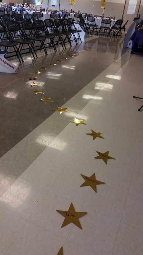 an empty room with chairs and gold stars on the floor, in front of a row of tables