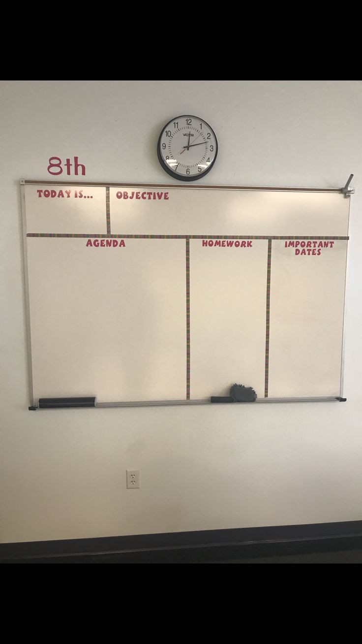 a clock mounted to the side of a wall above a white board with writing on it