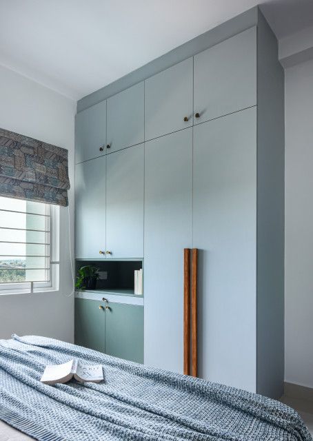 a bed sitting under a window in a bedroom next to a dresser and cupboards