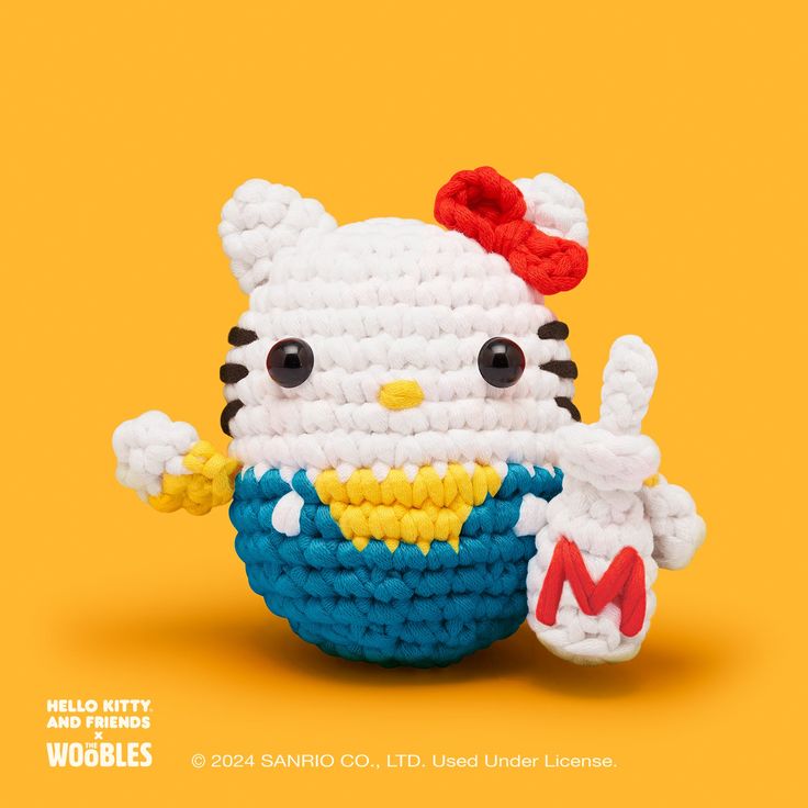 a crocheted hello kitty doll holding a mcdonald's burger king sandwich in it's mouth