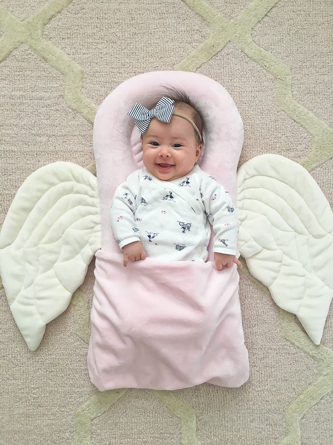 a baby laying on top of a pink blanket next to an angel wings shaped pillow