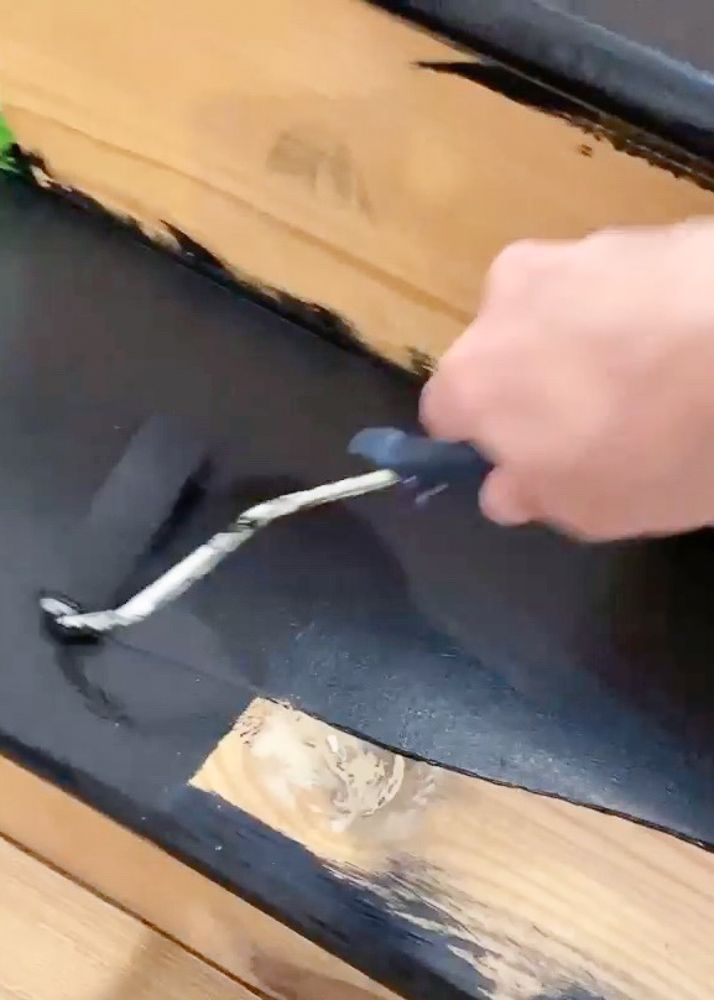 a person using a tool to paint the side of a piece of wood with black paint