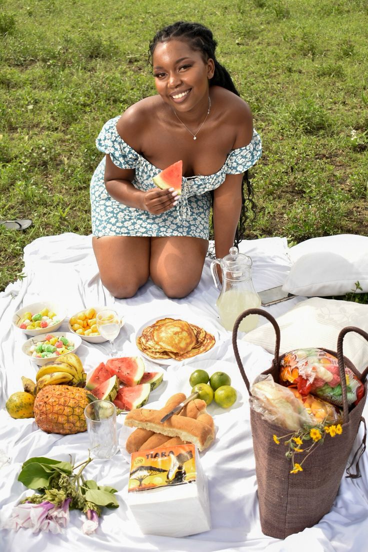 a woman sitting on a blanket with food in front of her and smiling at the camera