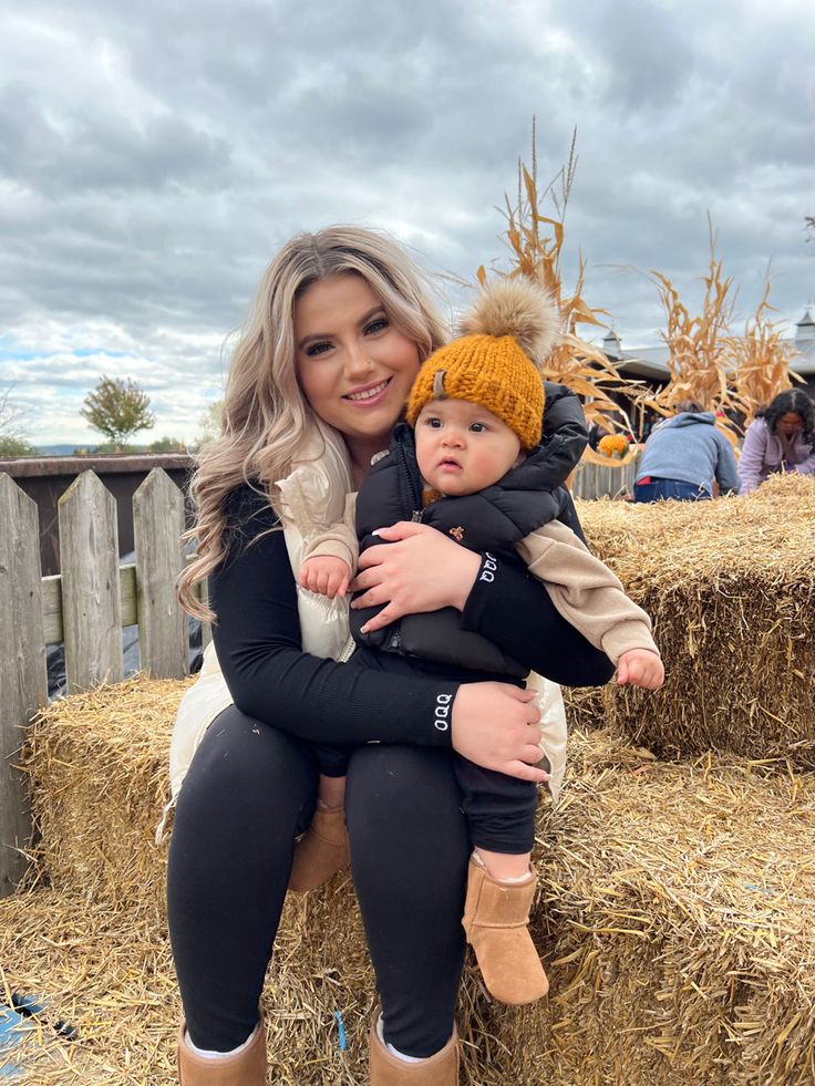 a woman holding a baby on top of hay bales