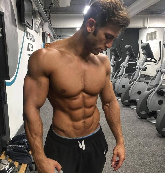 a shirtless man standing in front of a row of treadmills with his hands on his hips