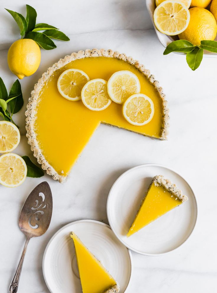 two slices of lemon tart on plates next to sliced lemons and limes