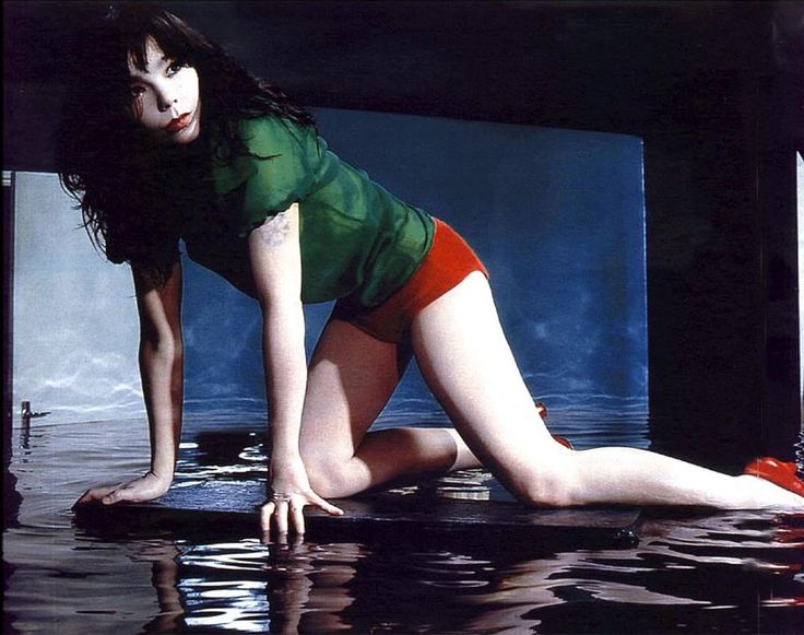 a woman in green shirt and red shorts laying on top of a body of water