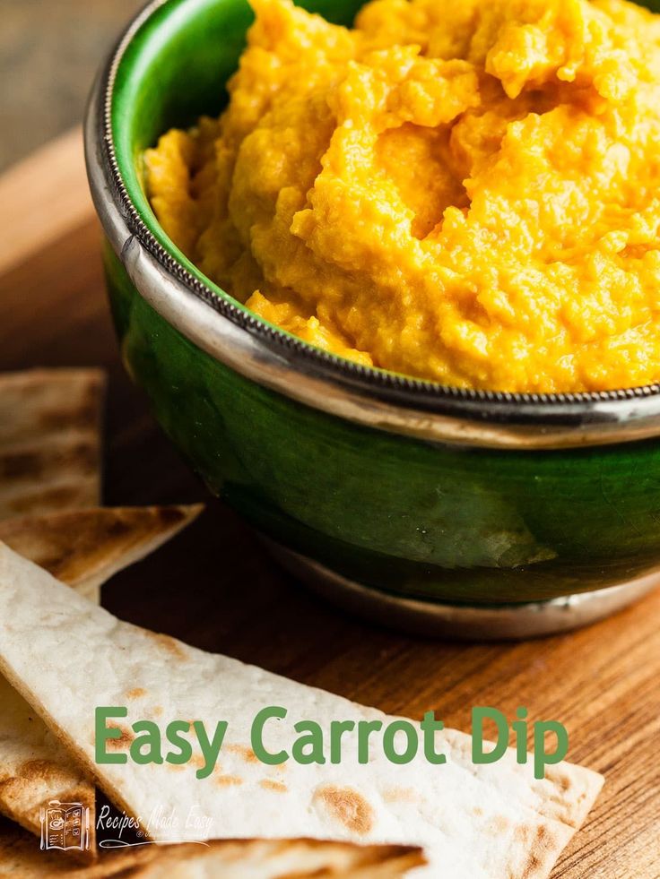 a green bowl filled with carrot dip next to tortilla chips