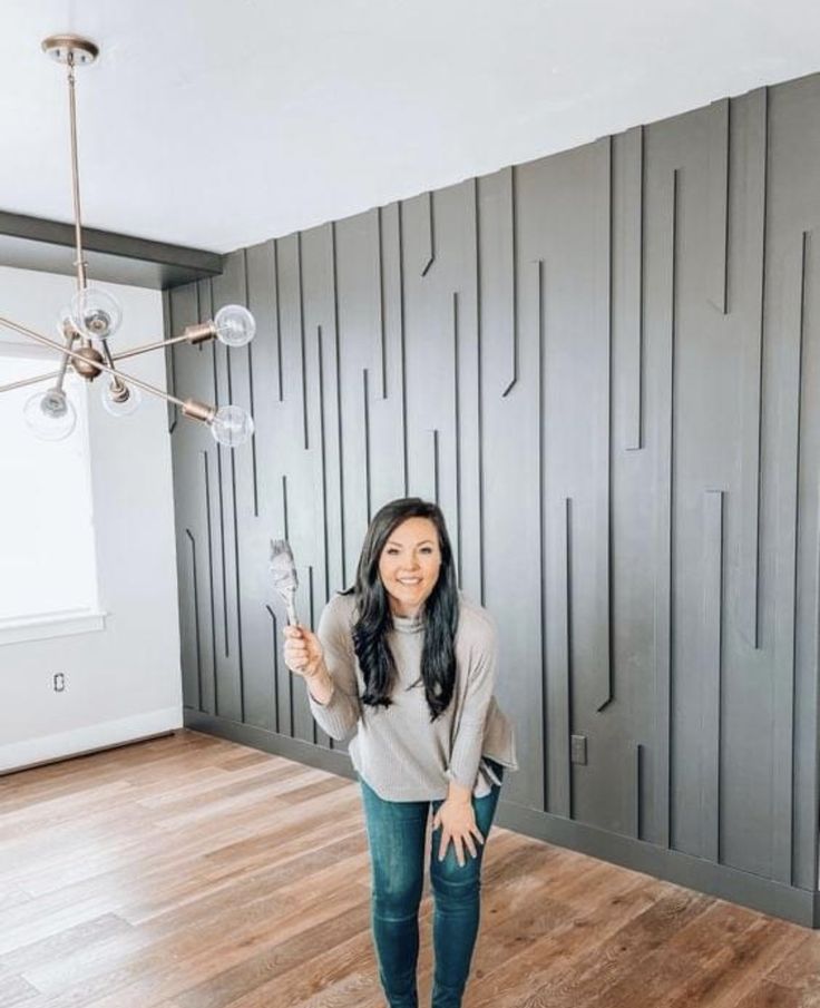 a woman standing in front of a wall with gray paneled walls and wooden floors