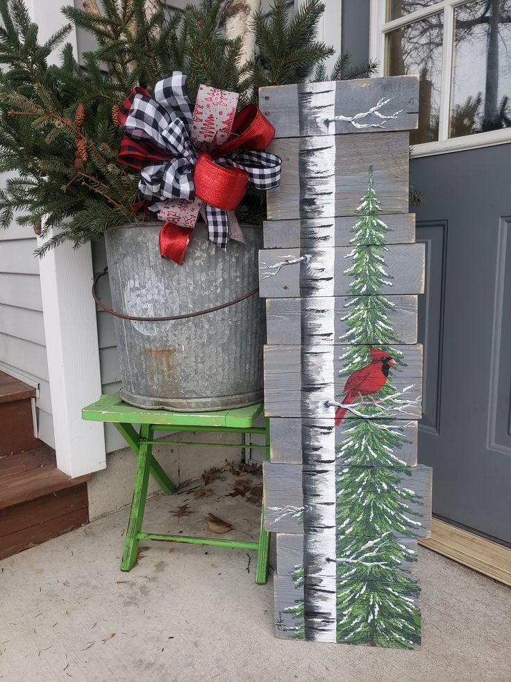 a metal bucket with a christmas tree and cardinal painted on it next to a wooden block