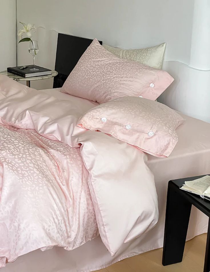 a bed with pink comforter and pillows on it in a room next to a table