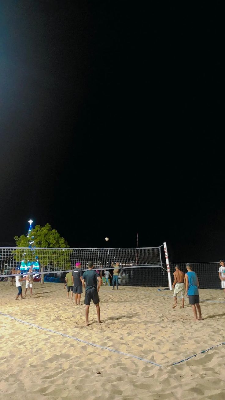 people playing volleyball on the beach at night