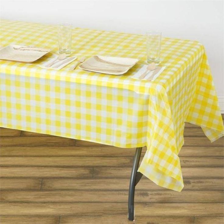 a yellow and white checkered tablecloth with place settings on it, sitting on a wooden floor