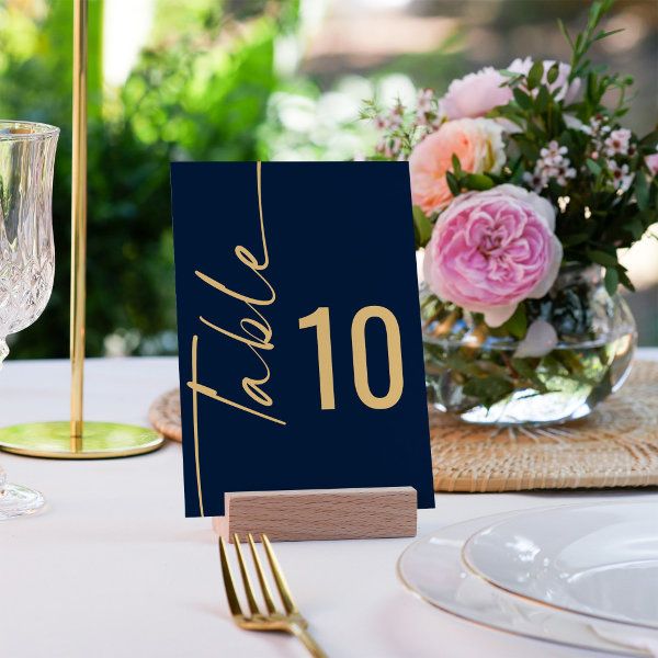 a table setting with place cards and flowers in vases on the table, along with gold cutlery