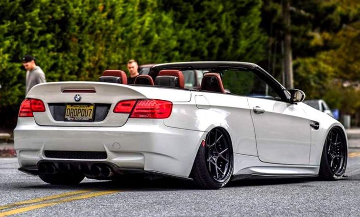 a white bmw convertible parked on the side of the road with people in the back seat