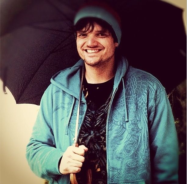 a man holding an umbrella in his hand and smiling at the camera while wearing a blue hoodie