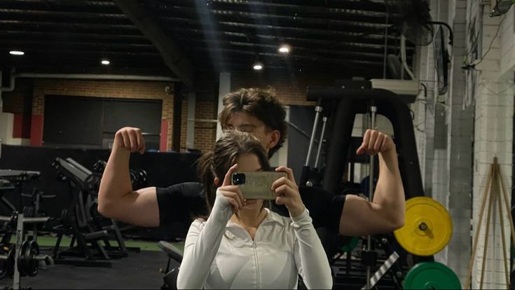 a man and woman taking a selfie in a gym with their hands up to the camera