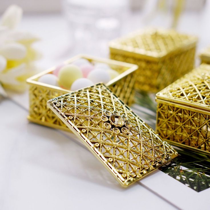 decorative gold boxes sitting on top of a table next to white flowers and candlesticks