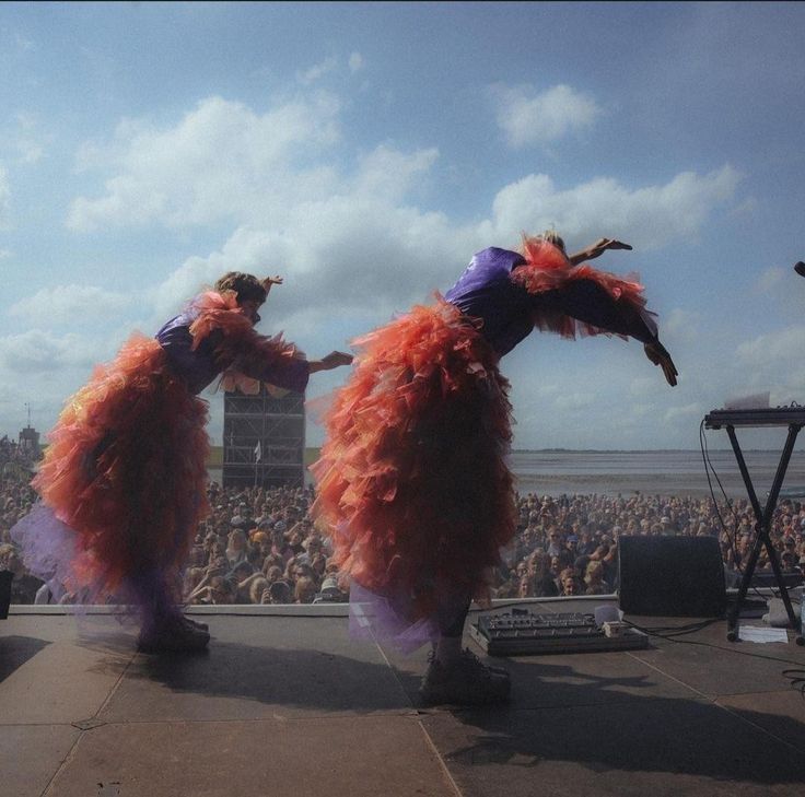 two people dressed in orange and purple dancing on stage