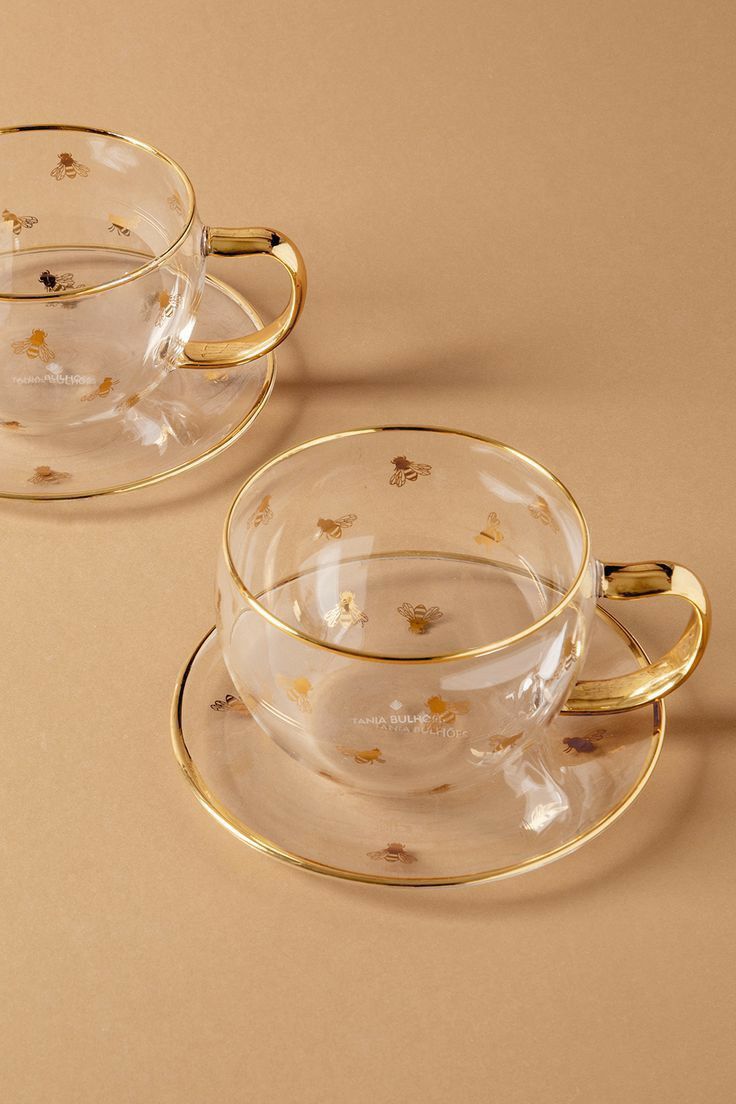 two clear tea cups with gold rims and saucers on a beige background,