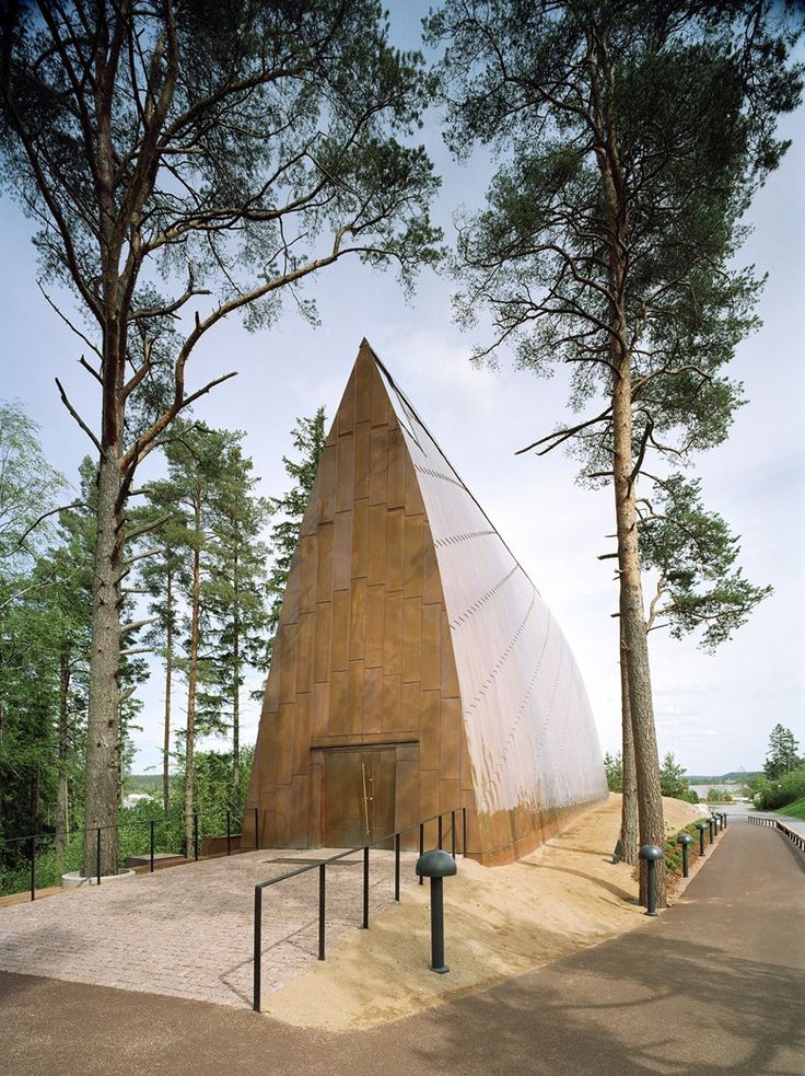 a triangular shaped building in the middle of a forest with trees around it and stairs leading up to it