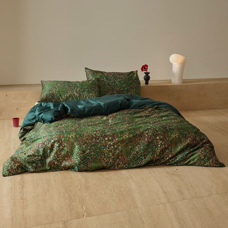 a bed with green sheets and pillows on the floor next to a vase filled with flowers