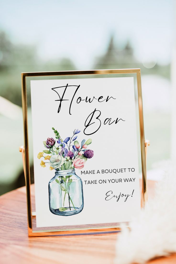 a flower bar sign sitting on top of a wooden table next to a glass vase filled with flowers