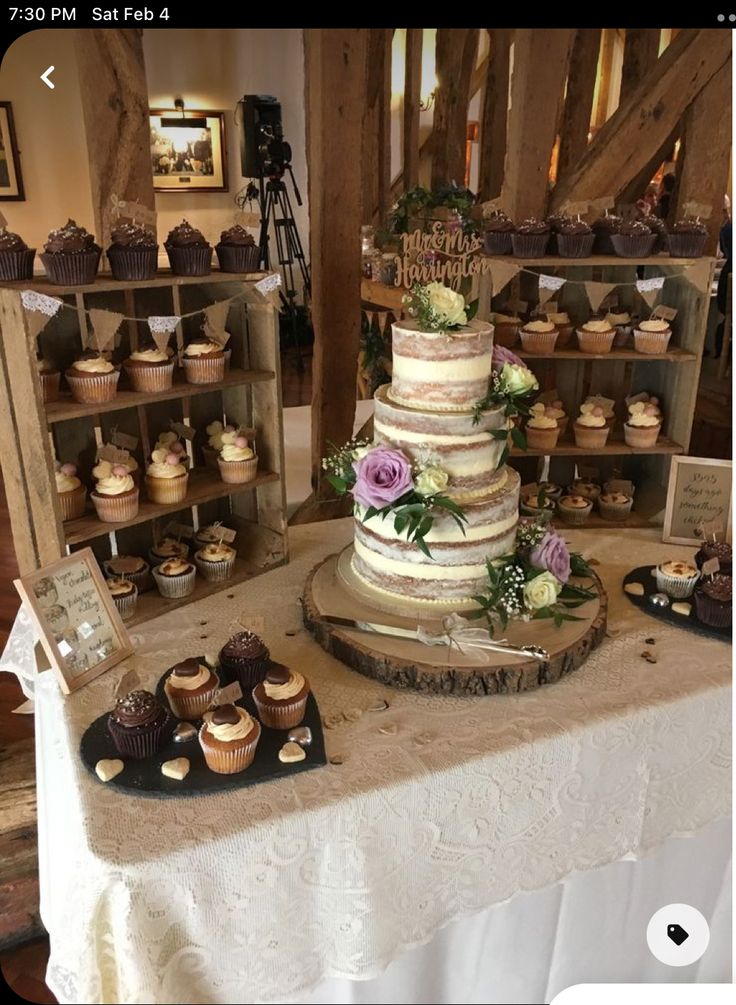 a table topped with lots of cupcakes next to wooden shelves filled with cakes