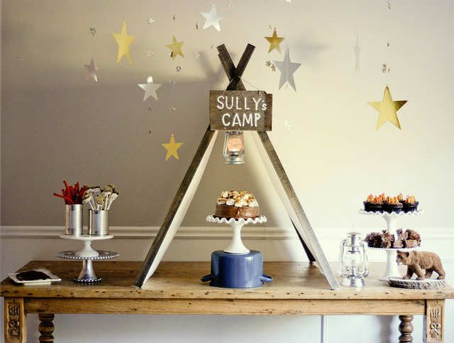 a table topped with cakes and cupcakes next to a teepeel tent