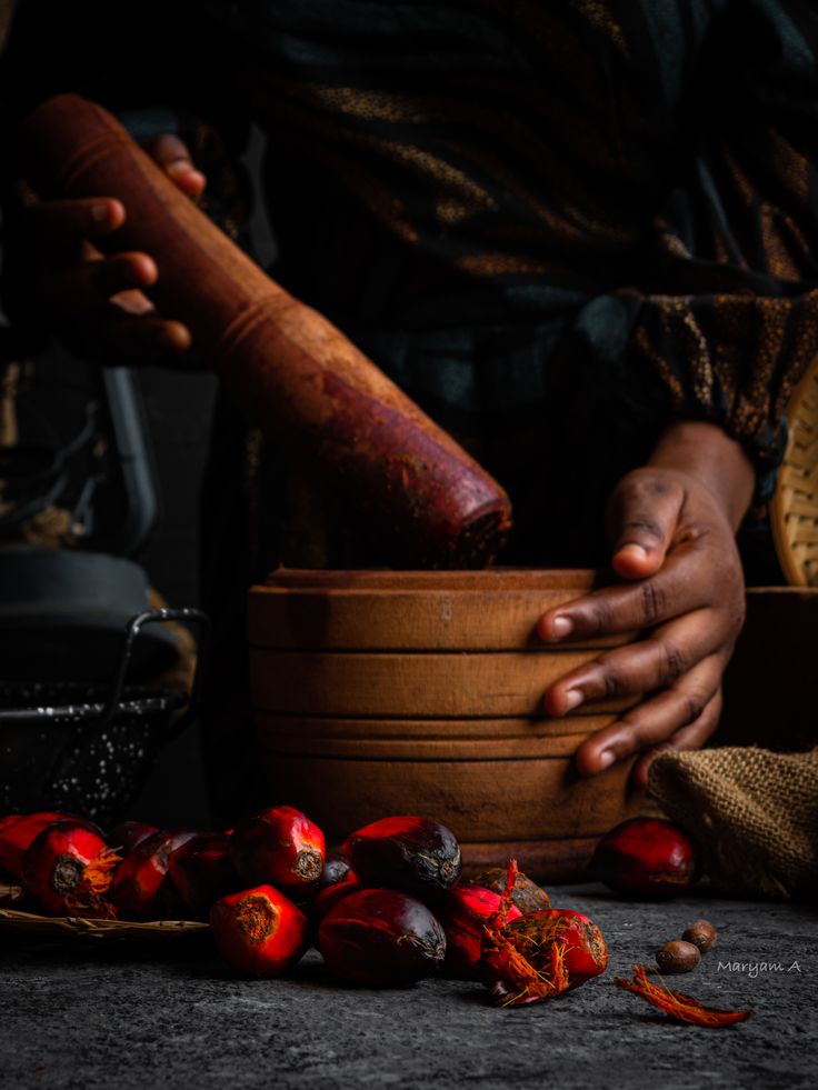 a person holding a wooden bowl filled with red peppers next to other food items on a table