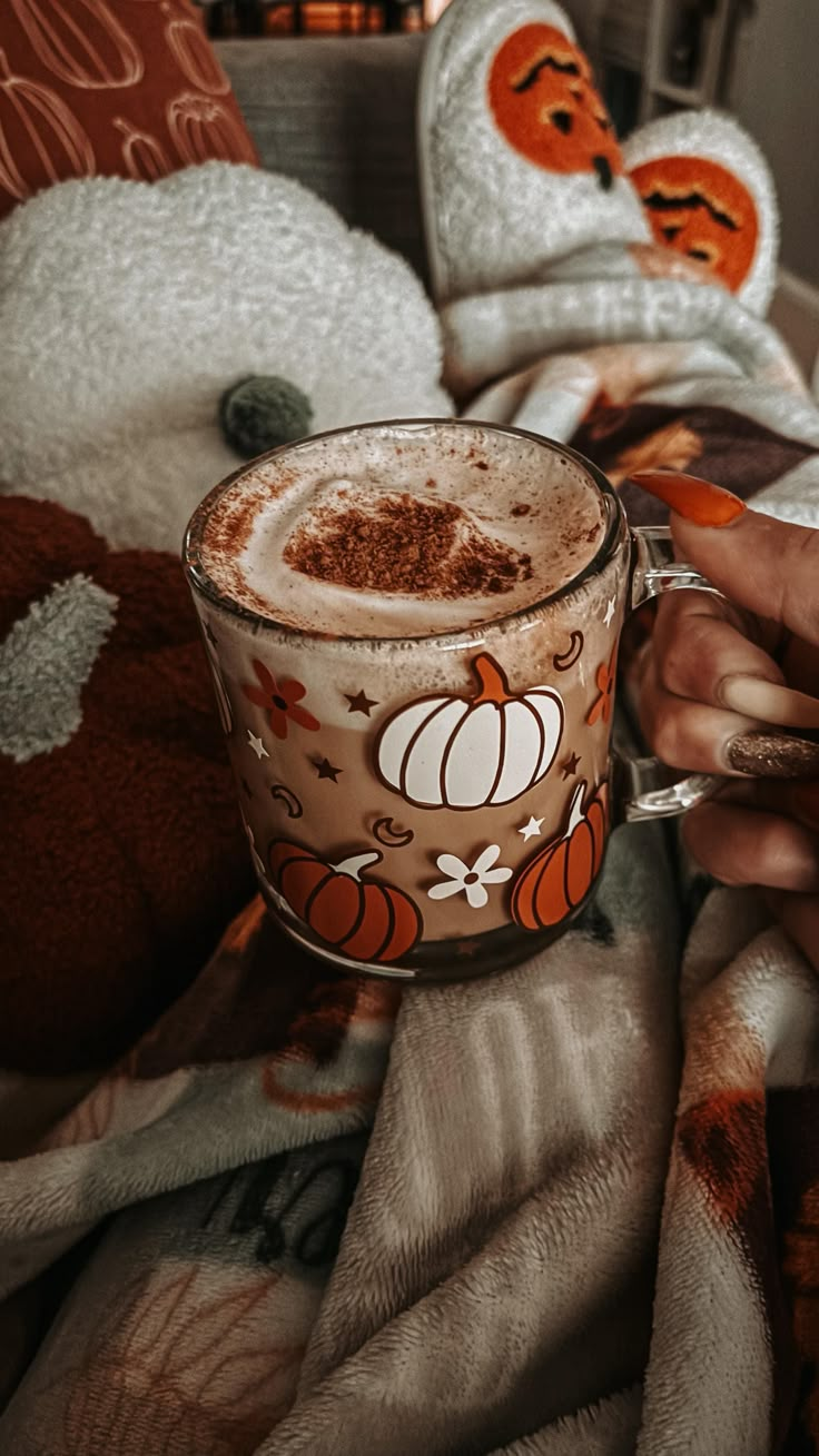 someone is holding a cup of hot chocolate in their hand while sitting on a bed