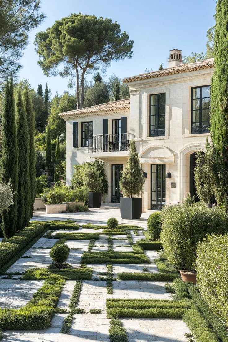 a large white house surrounded by trees and bushes in the middle of a garden area