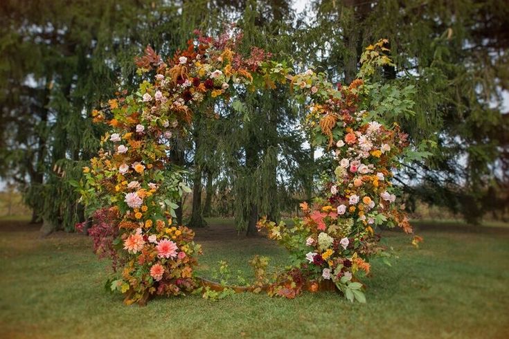 an arch made out of flowers in the middle of a grassy area with trees behind it