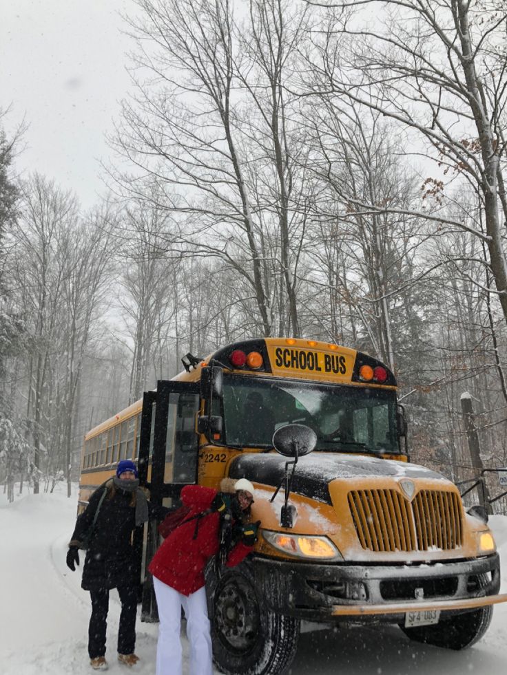 two people standing next to a school bus in the snow