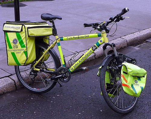 a yellow bicycle parked next to a street with a green bag on the handlebars